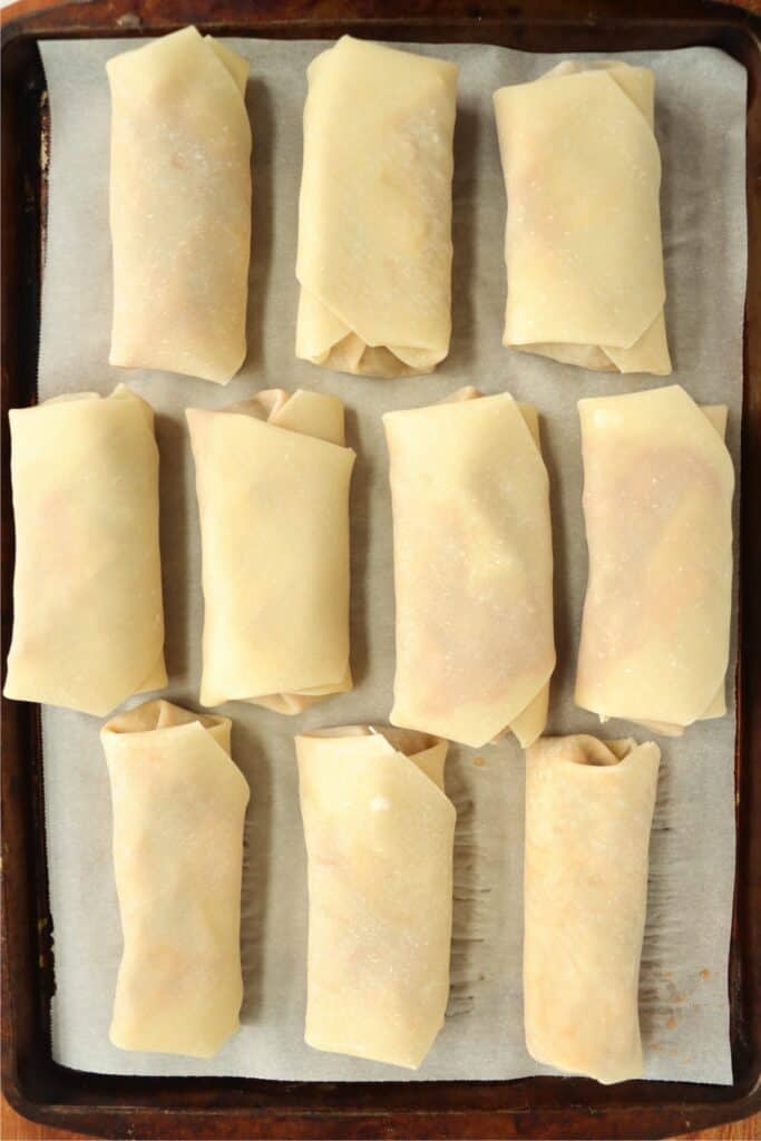 Overhead shot of taco egg rolls on baking sheet lined with parchment paper. 