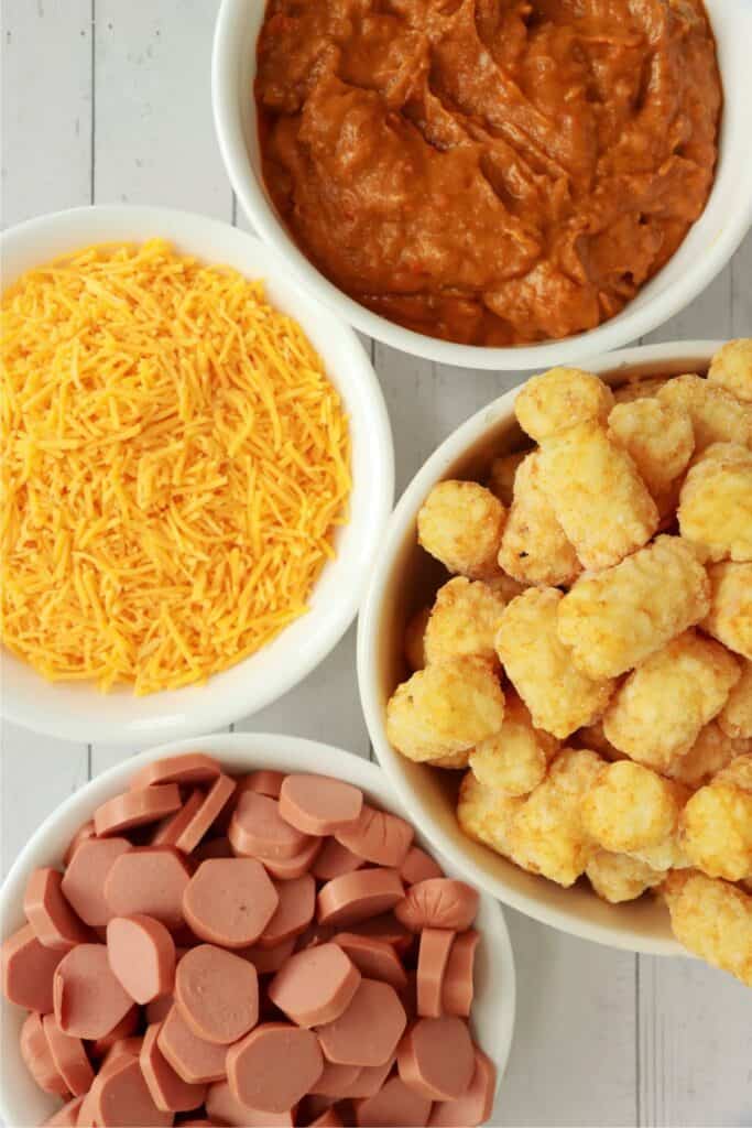 Overhead shot of individual chili cheese dog tater tot casserole ingredients in bowls