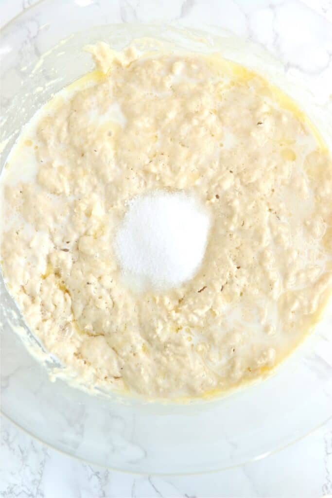 Overhead shot of sugar, butter, and salt added to dough mixture in bowl