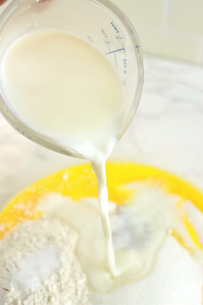 Milk being poured into mixing bowl with eggs, flour, vanila, sugar, and salt. 