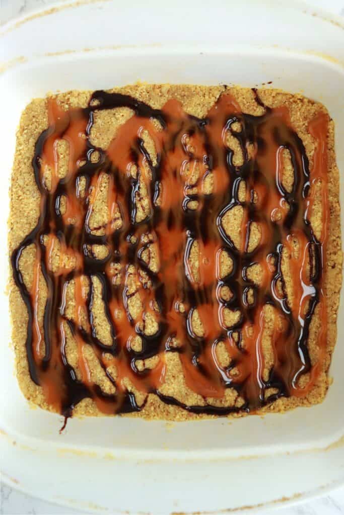 Overhead shot of drumstick ice cream cake crust drizzled with chocolate and caramel sauce in dish. 