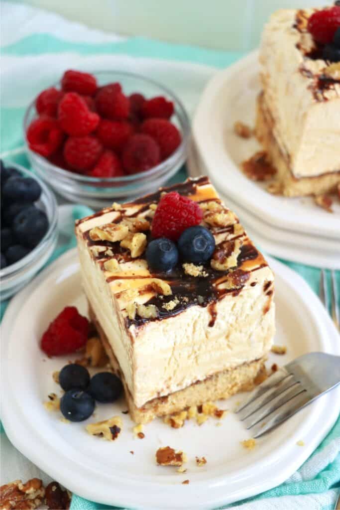 Two slices of drumstick ice cream cake on plates next to bowls of raspberries and strawberries