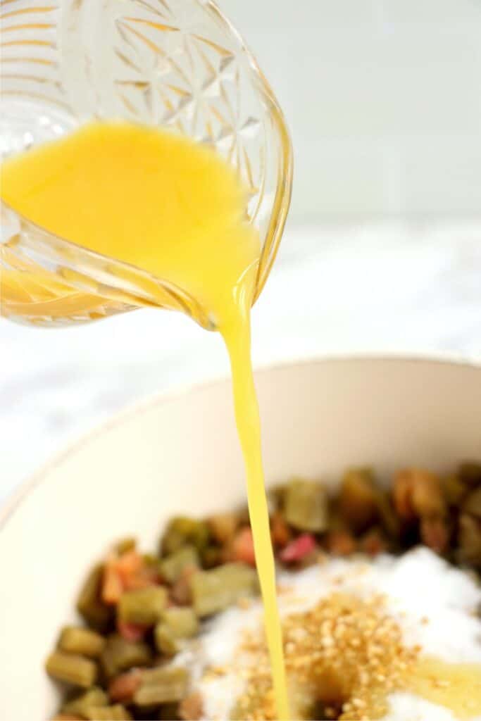 Orange juice being poured into pot of rhubarb, sugar, and orange zest.