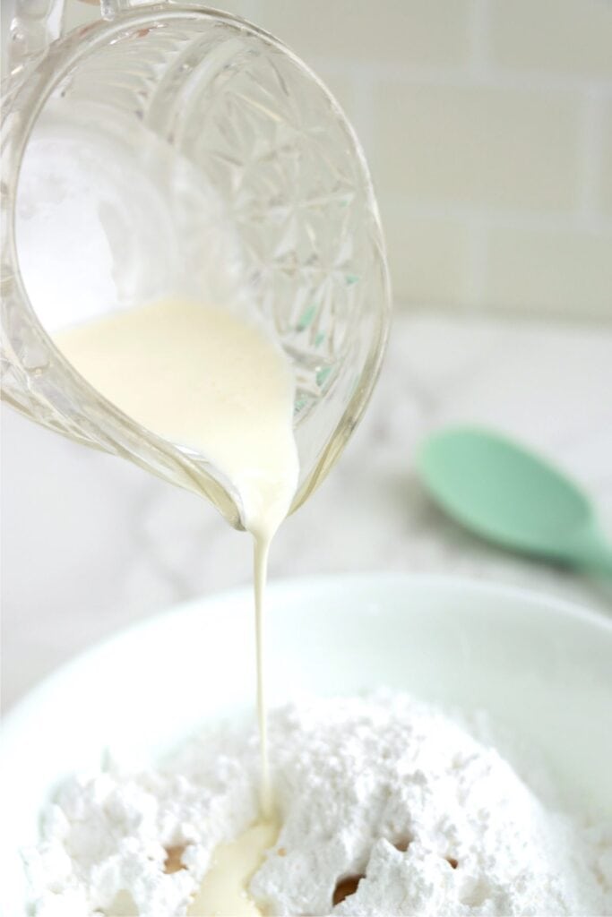 Heavy whipping cream being poured into bowlful of powdered sugar.