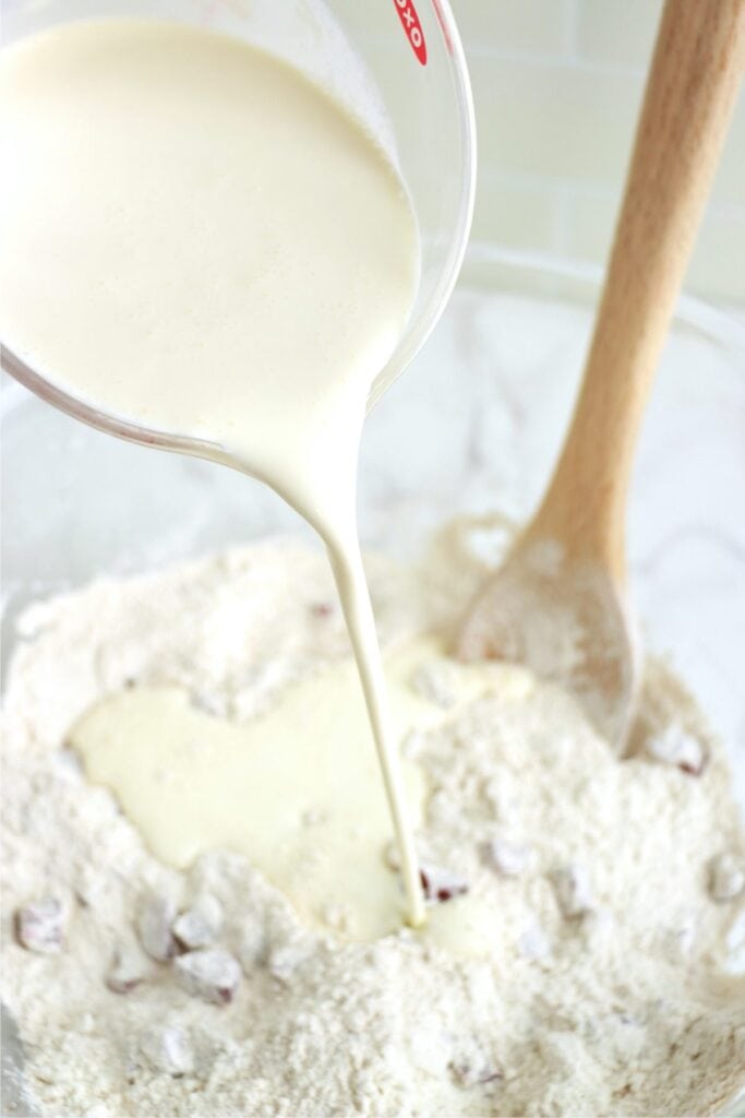 Heavy whipping cream being poured into dry scone dough ingredients