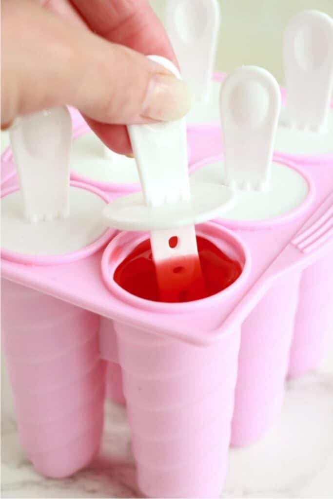 Popsicle insert being placed into popsicle mold full of Kool Aid