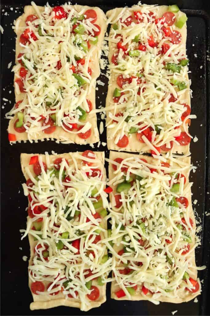 Overhead shot of four crescent dough rectangles on baking sheet topped with cheese, pepperoni, and diced bell pepper