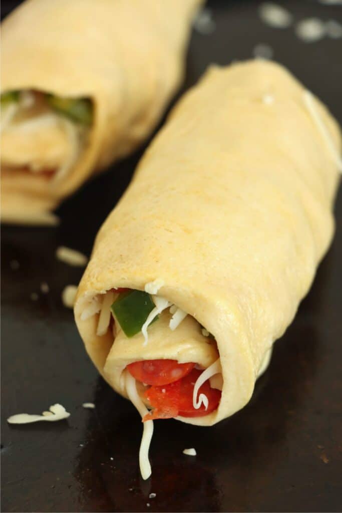 Closeup shot of crescent dough with pizza toppings rolled into a log.