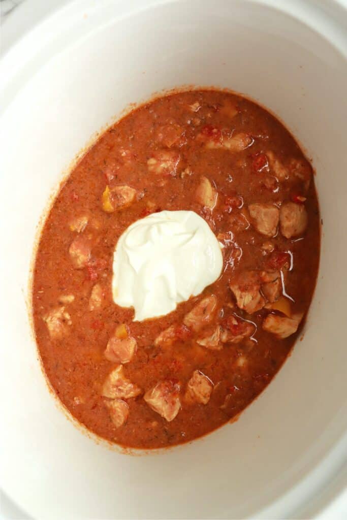 Overhead shot of sour cream in slow cooker full of chicken paprikash