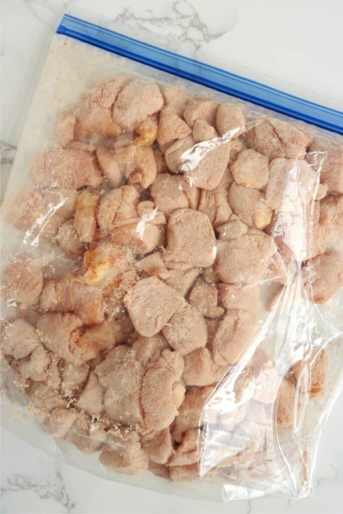 Overhead shot of chicken coated in flour and paprika in resealable bag.