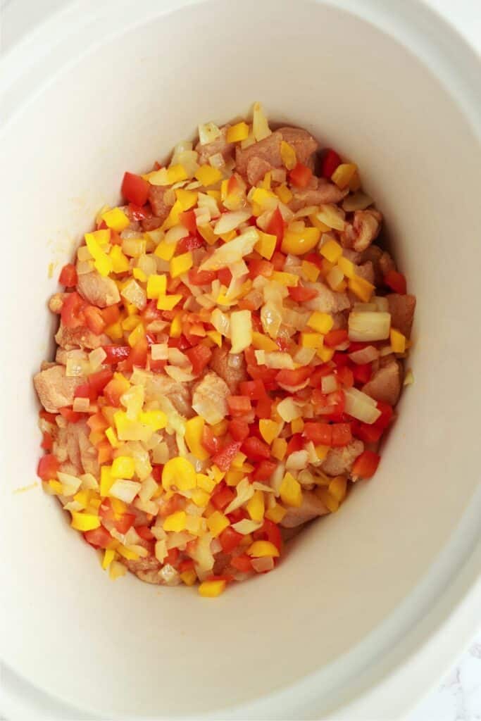 Overhead shot of onions, peppers, and cubed chicken in slow cooker