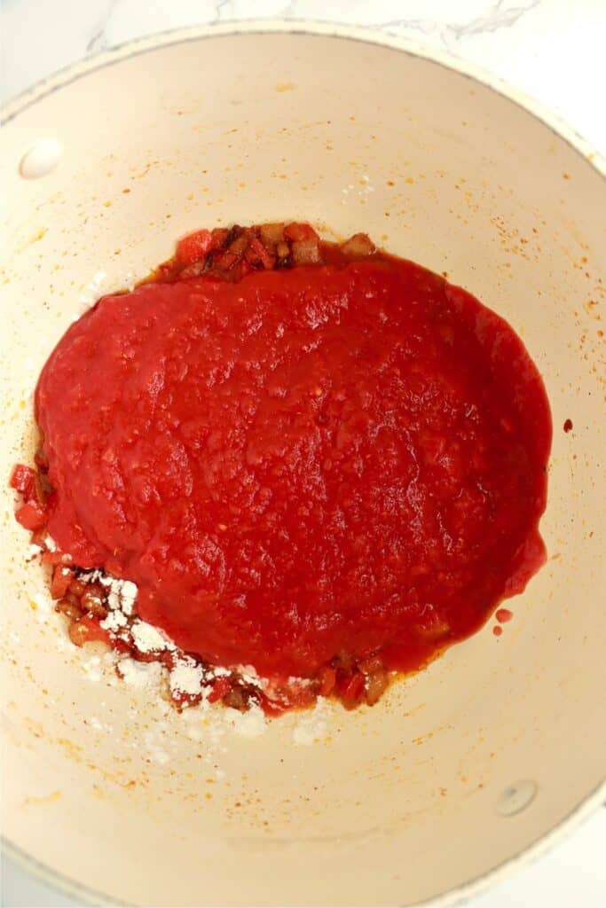 Overhead shot of vegetables and cornstarch mixture with crushed tomatoes in skillet