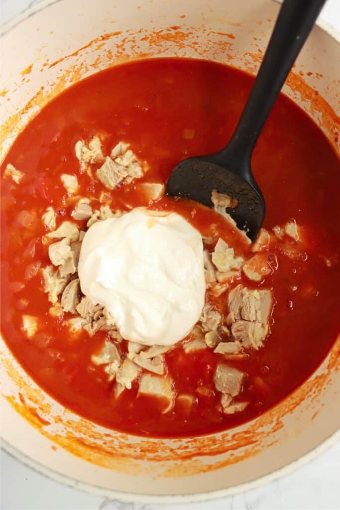 Overhead shot of chicken and sour cream being mixed into soup