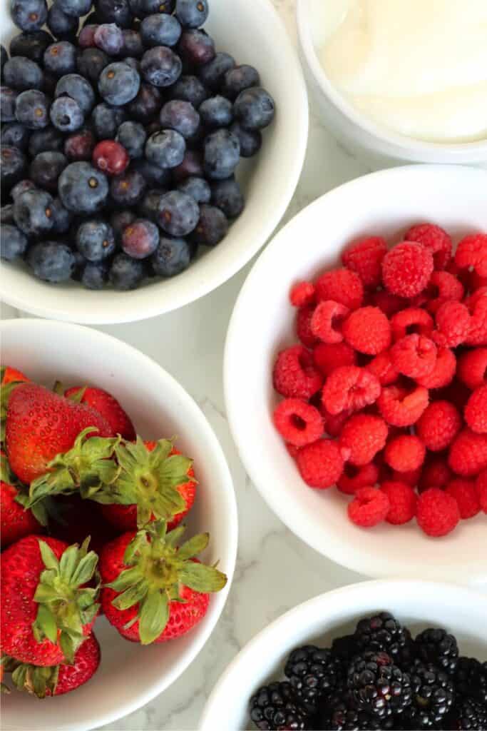 Overhead shots of bolwfuls of blueberries, raspberries, blackberries, and strawberries on table. 