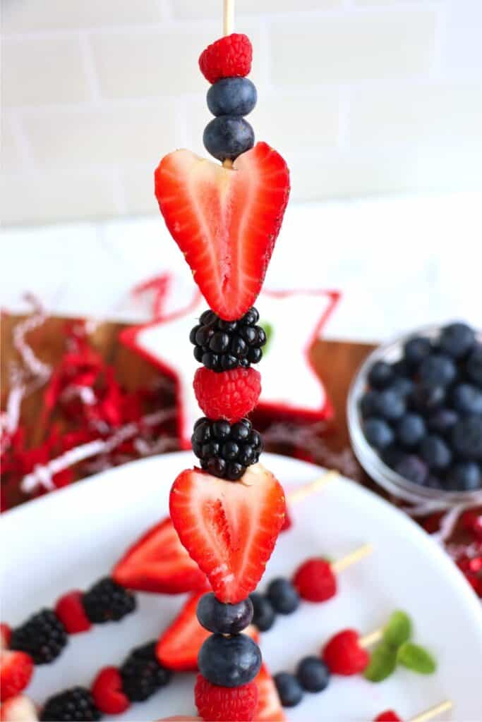 Closeup shot of 4th of July fruit kabob over plate of more kabobs.