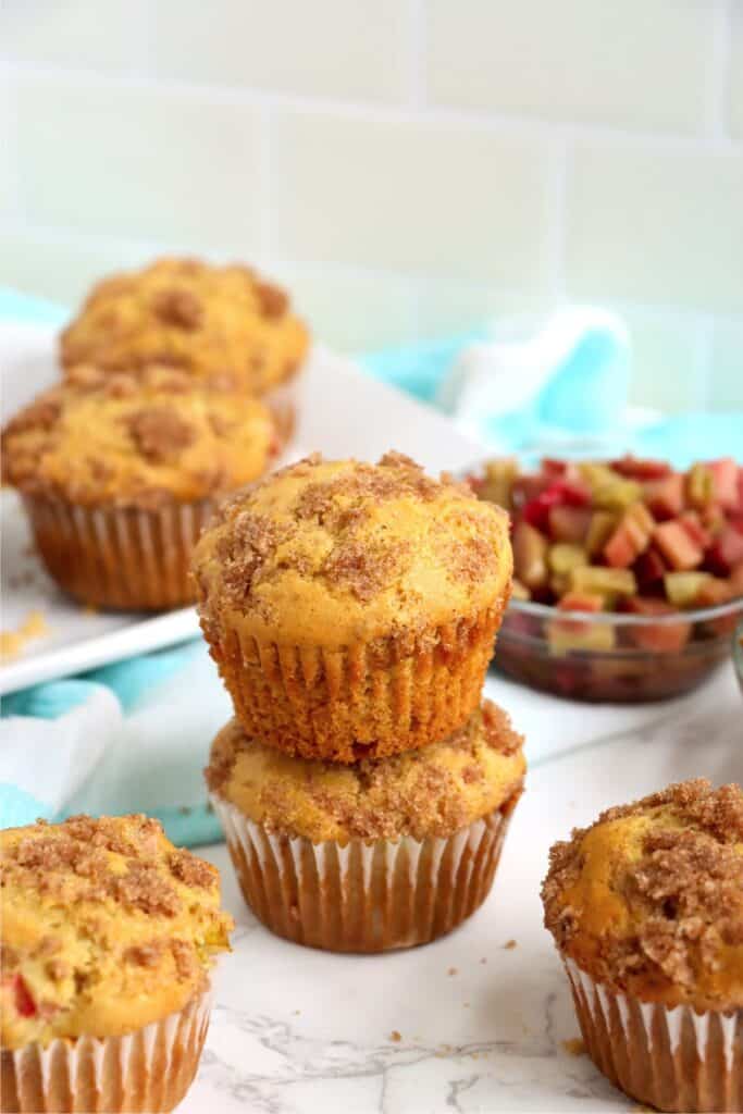 Closeup shot of two homemade rhubarb muffins stacked atop one another with more muffins in background. 