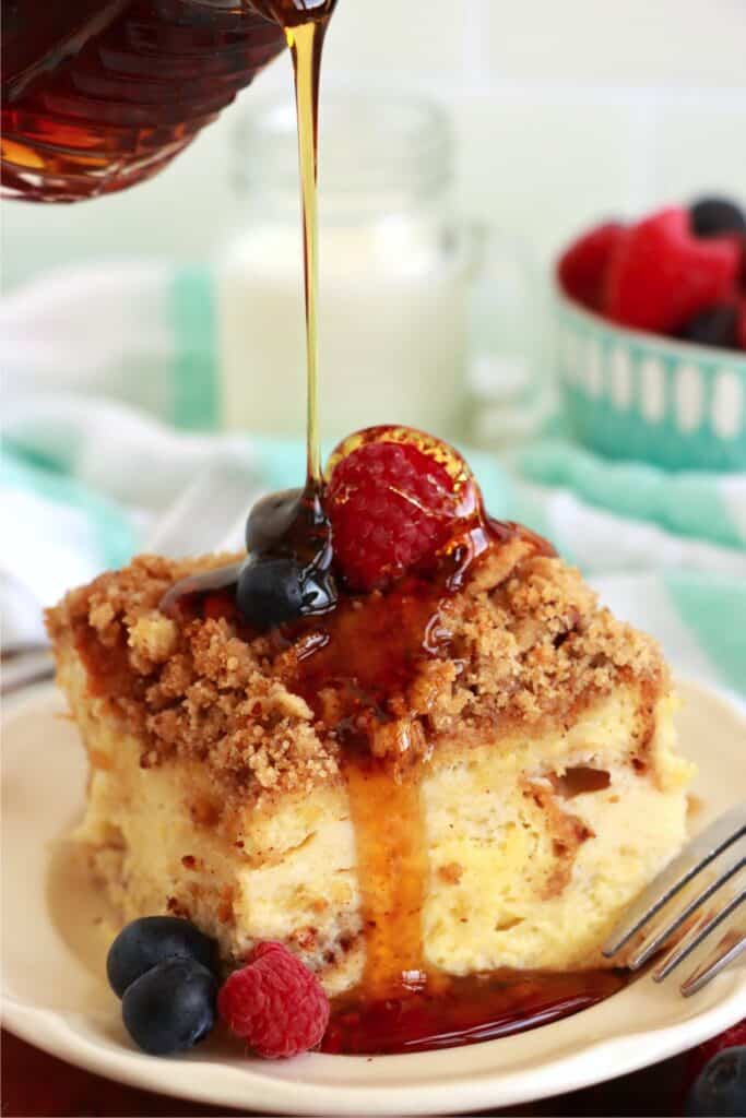 Closeup shot of slice of cream cheese stuffed French toast topped with blueberries and raspberries being drizzled with syrup.