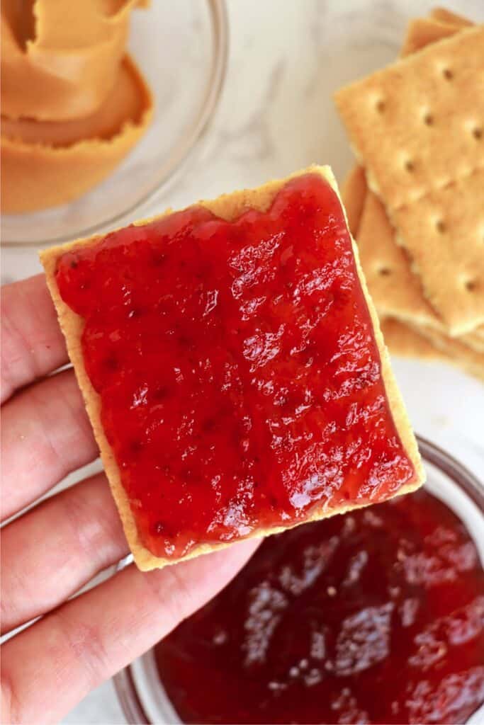 Overhead shot of hand holding a graham cracker square topped with jelly.