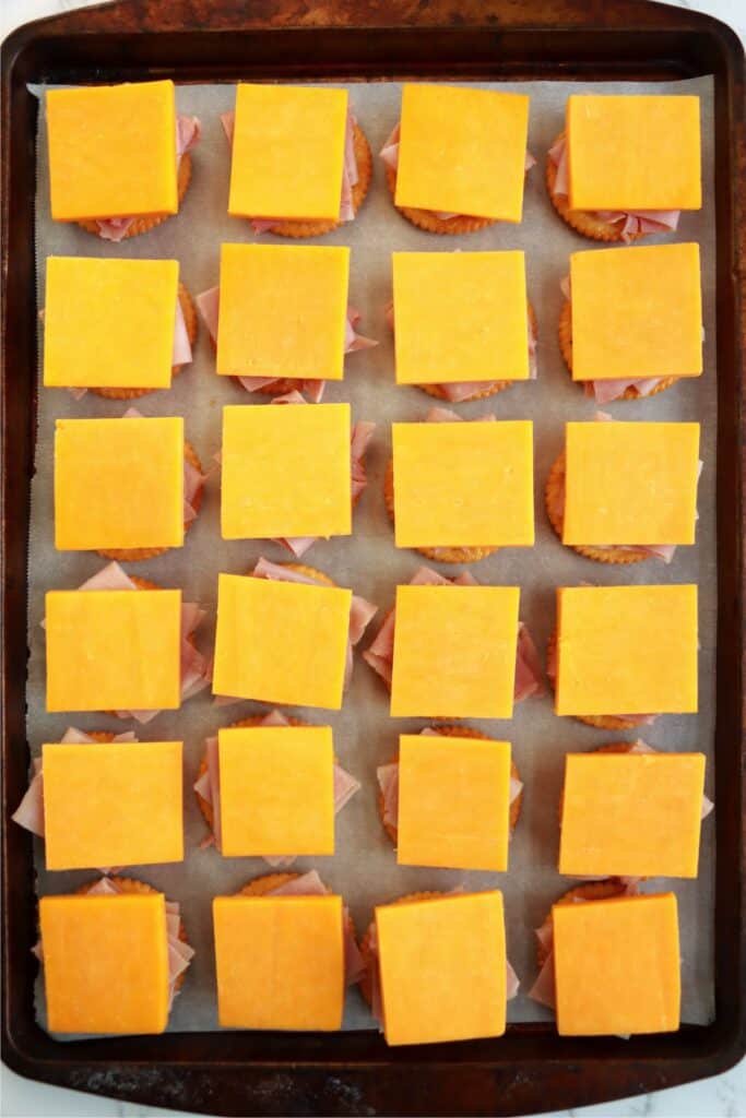 Overhead shot of baking sheet with Ritz crackers topped with ham and cheese.