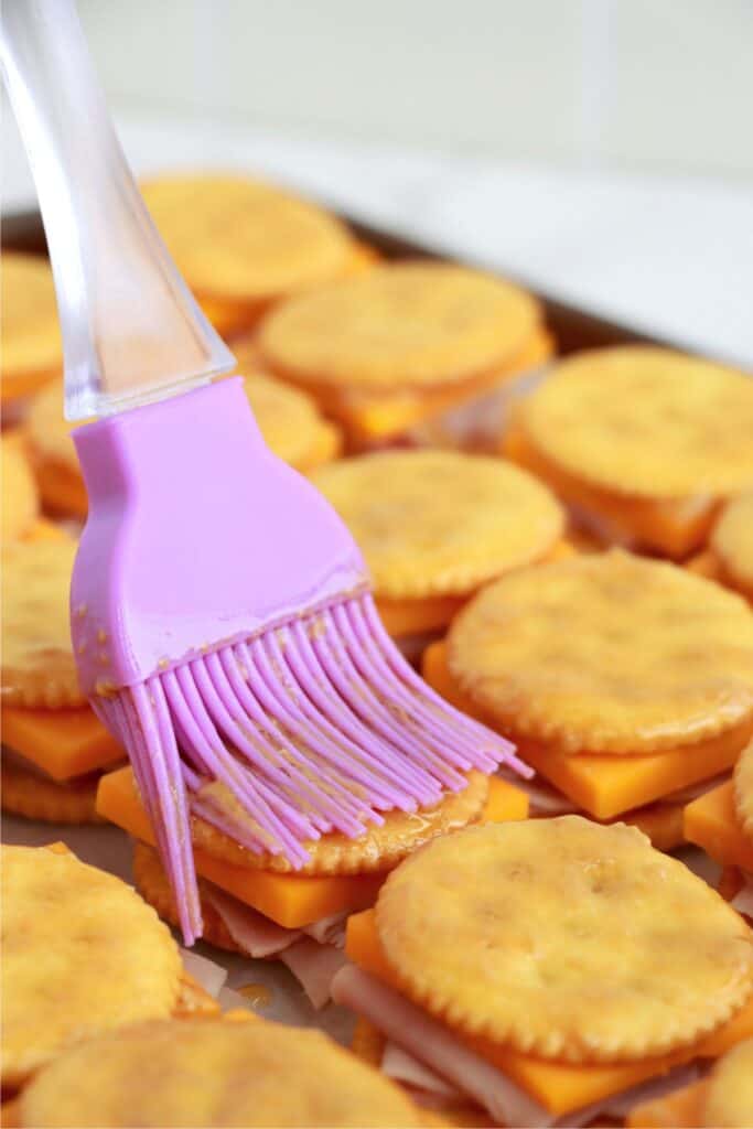 Closeup shot of Ritz cracker sandwiches being brushed with honey mustard mixture. 