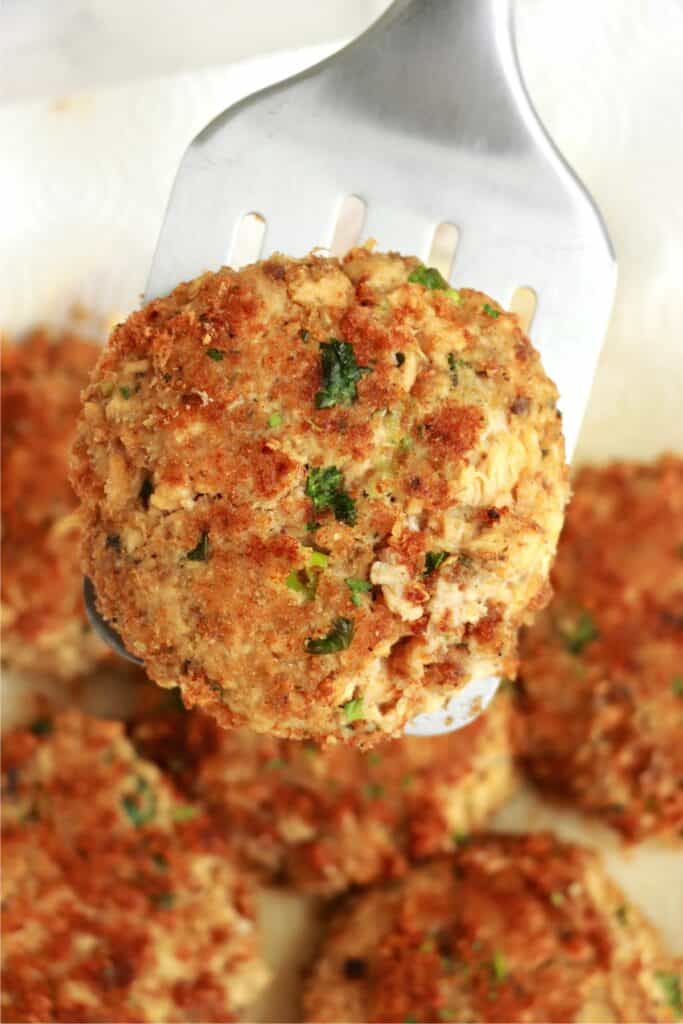 Closeup shot of spatula with salmon patty over plate of more easy salmon patties