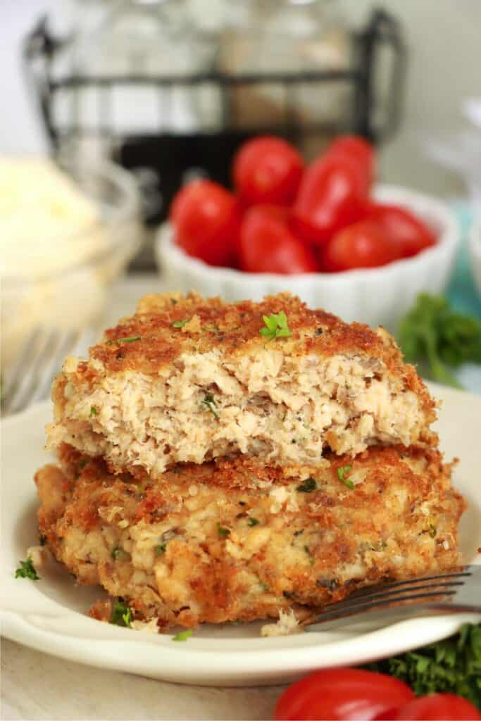 Closeup shot of two salmon patties stacked atop one another on plate with top patty cut in half.