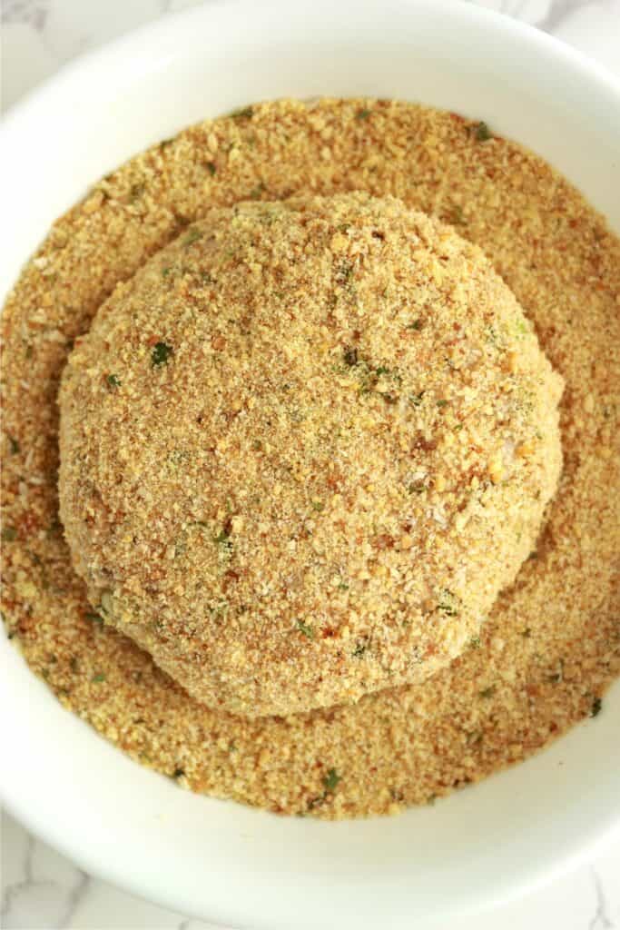 Overhead shot of salmon patty in plate of breadcrumbs.