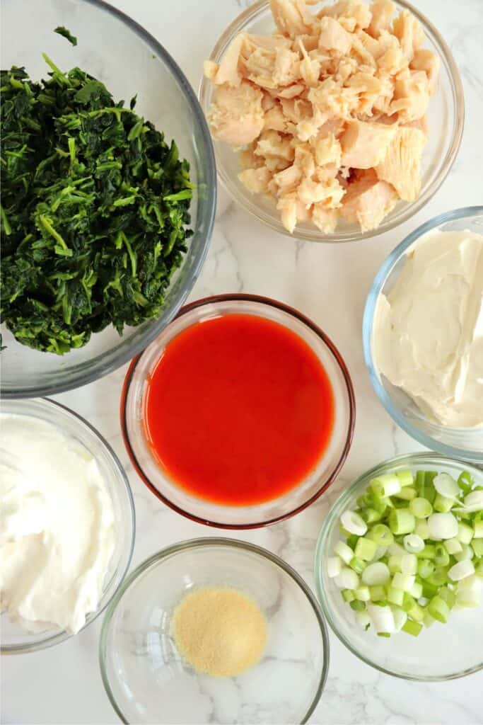 Overhead shot of individual Buffalo chicken spinach dip ingredients in bowls