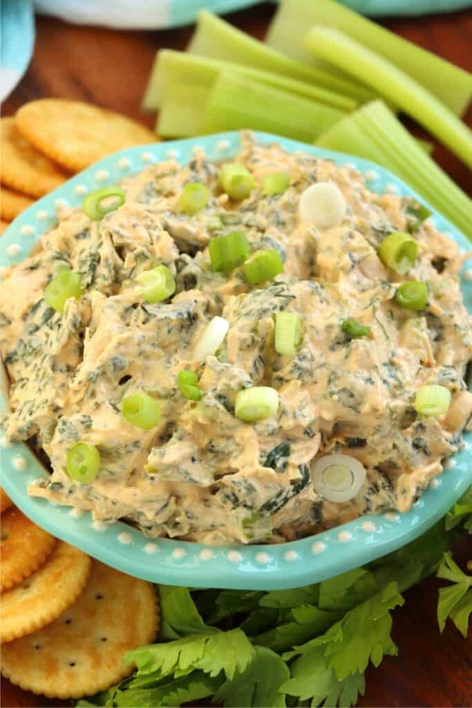 Closeup shot of bowlful of Buffalo chicken spinach dip surrounded by crackers and celery