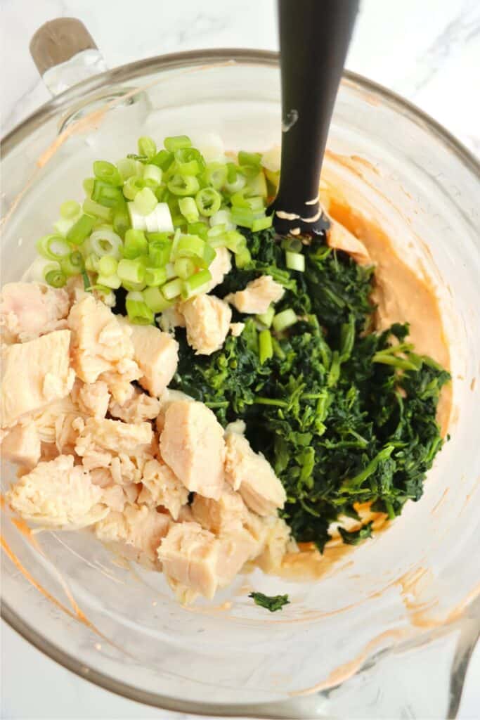 Overhead shot of canned chicken, onions, and spinach in bowlful of Buffalo sauce.