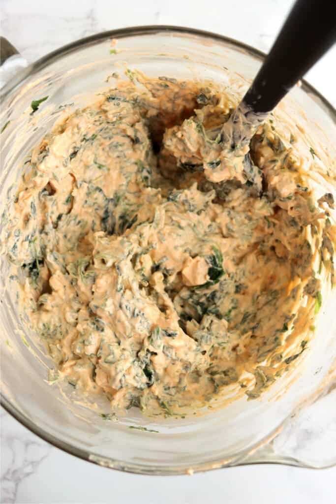 Overhead shot of large spoon mixing Buffalo chicken spinach dip in mixing bowl