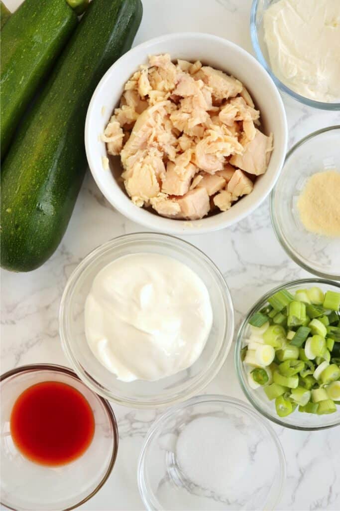 Overhead shot of Buffalo chicken zucchini boat ingredients in individual bowls on table