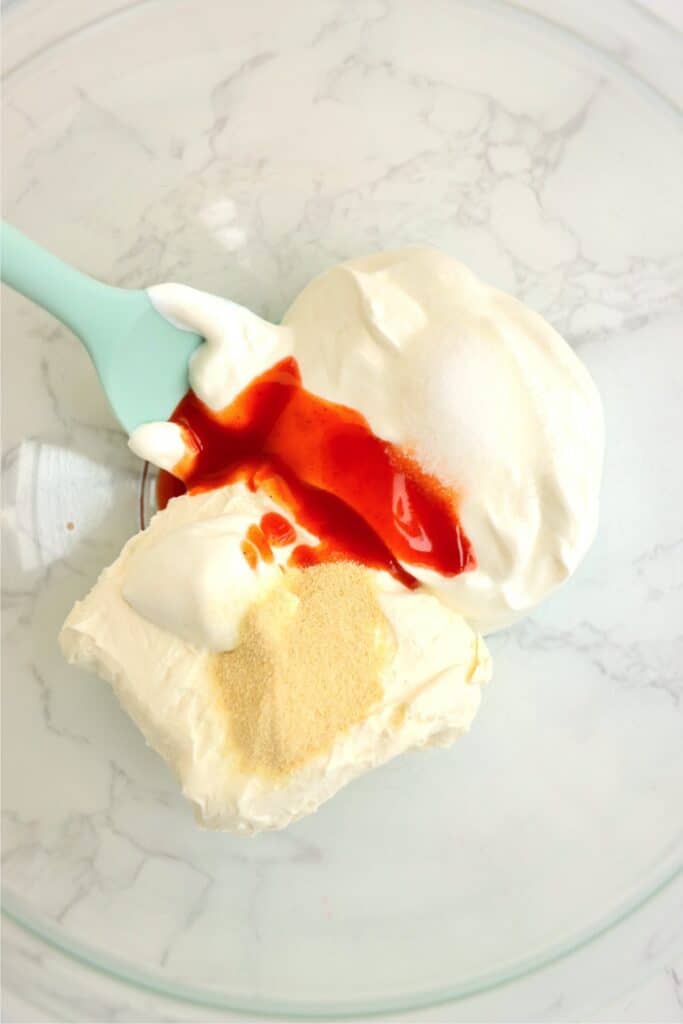 Overhead shot of sour cream, cream cheese, Buffalo sauce and seasonings in mixing bowl