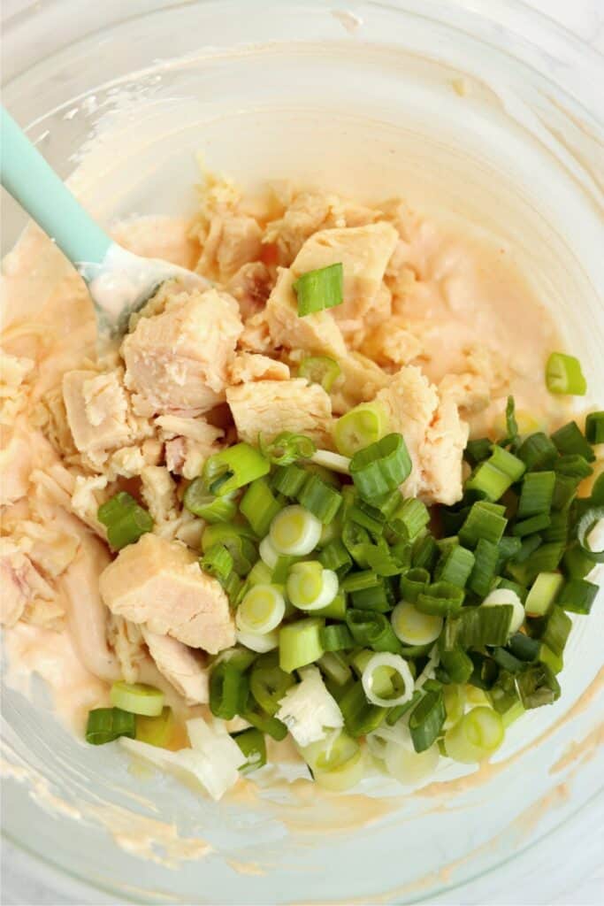 Overhead shot of chicken and chopped green onions on top of Buffalo sauce mixture in mixing bowl