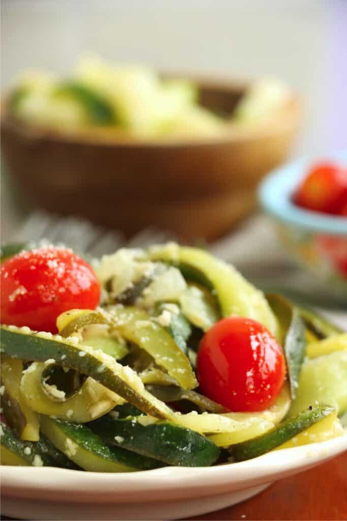 Closeup shot of plateful of caramelized zucchini with bowl of zucchini in background.