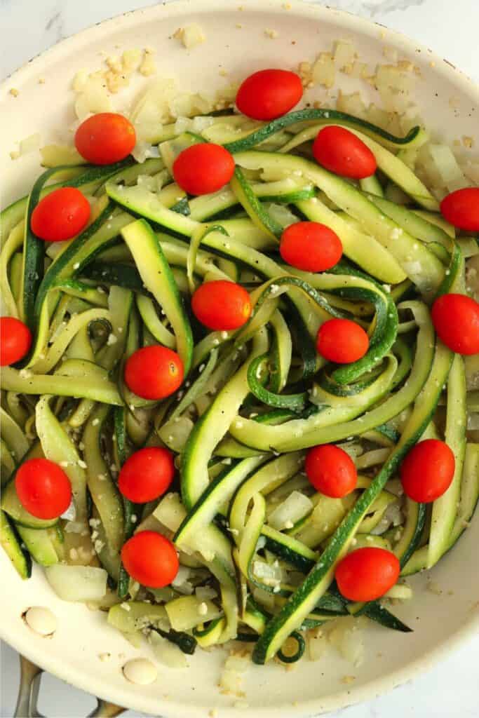 Overhead shot of zucchini, onions, garlic, and tomatoes in skillet. 