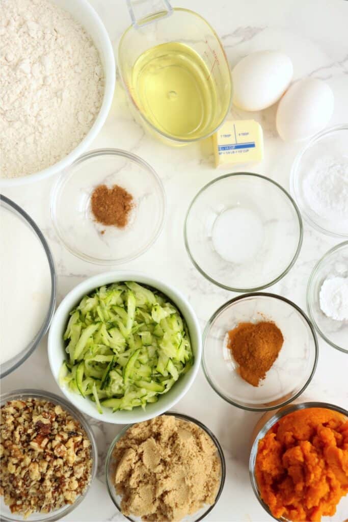 Overhead shot of pumpkin zucchini muffin ingredients in bowls