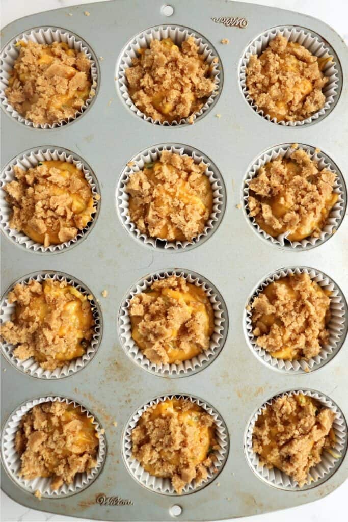 Overhead shot of unbaked pumpkin zucchini muffins with crumble topping in muffin tin