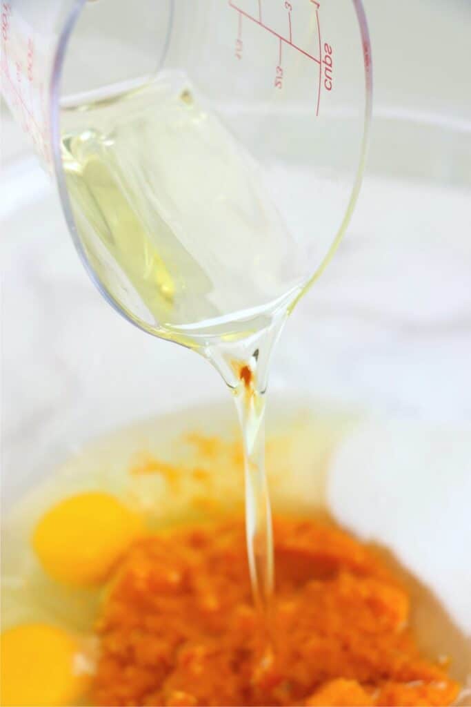 Closeup shot of oil being poured into mixing bowl with wet muffin ingredients.