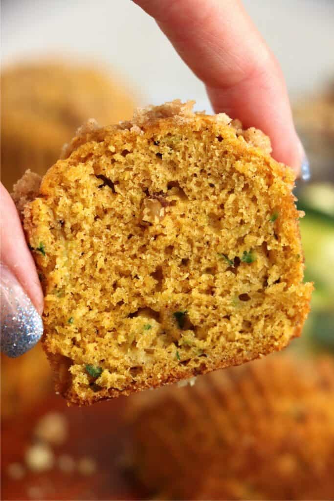 Closeup shot of hand holding half a pumpkin zucchini muffin.