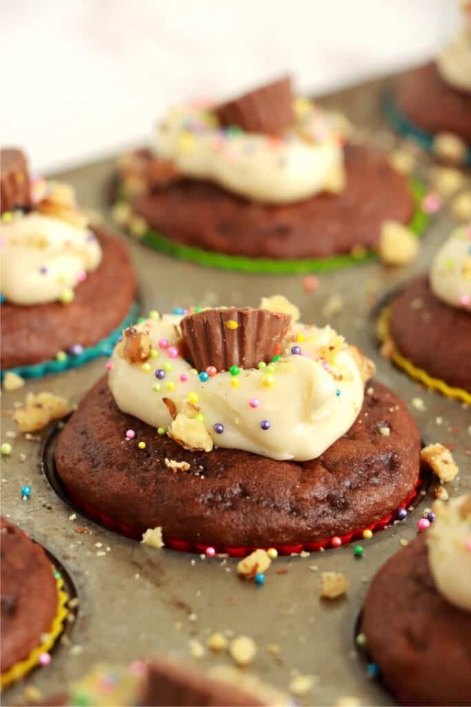 Closeup shot of cream cheese stuffed cupcakes topped with cream cheese frosting and mini peanut butter cup in muffin tin