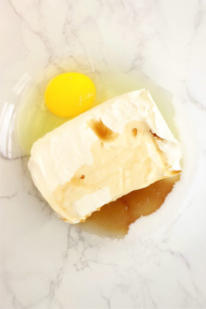 Overhead shot of cream cheese, egg, sugar, and vanilla in mixing bowl. 