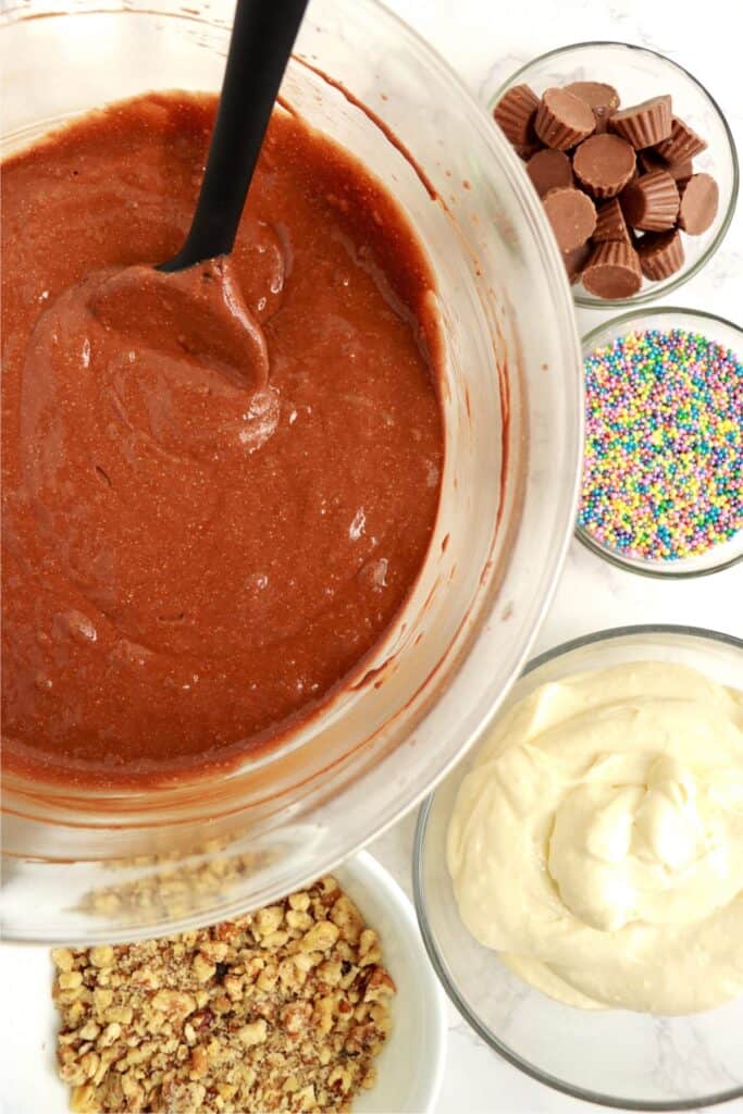 Overhead shot of cake batter in mixing bowl next to smaller bowls with other cupcake ingredients