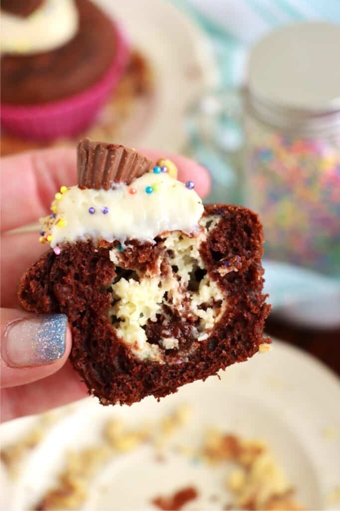 Closeup shot of hand holding half a cream cheese stuffed cupcake