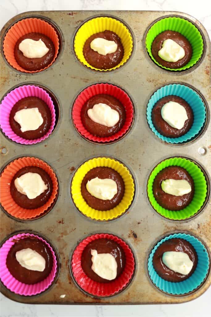 Overhead shot of chocolate cake batter in cupcake liners with spoonful of cream cheese filling on top