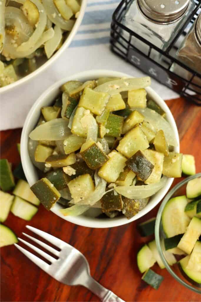 Overhead shot of bowlful of sauteed zucchini and onion next to another bowlful of uncooked zucchini