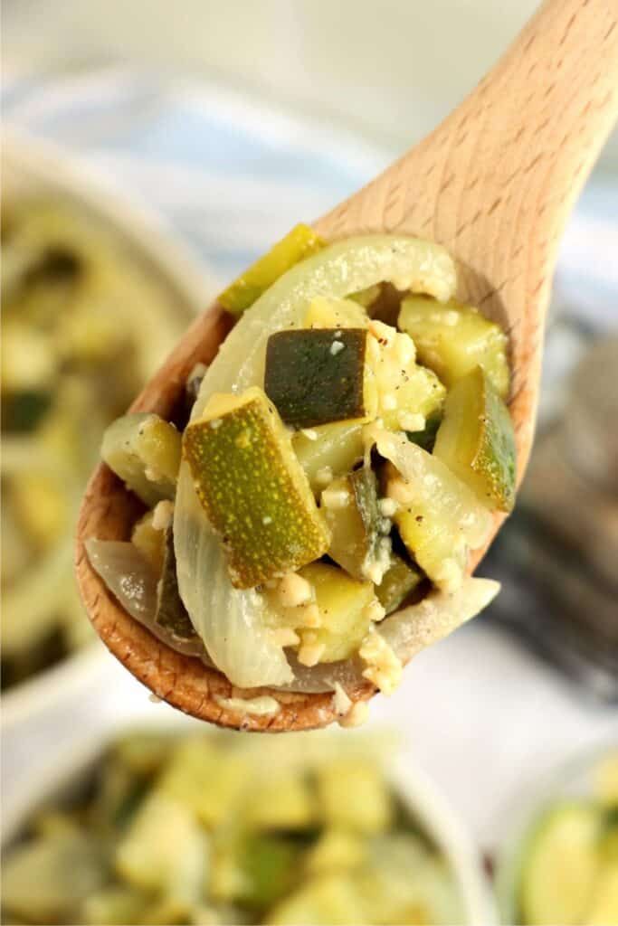 Overhead closeup shot of wooden spoon full of sauteed zucchini and onions. 