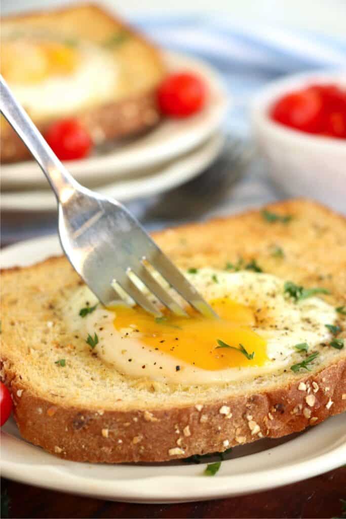 Closeup shot of fork cutting into an air fryer egg on toast on plate.