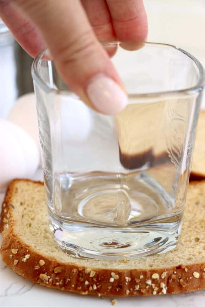 Closeup shot of glass being pressing into the center of a slice of bread. 