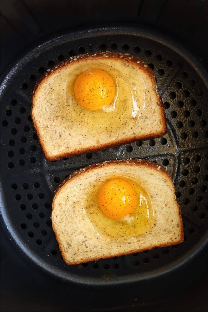 Overhead shot of eggs on bread in air fryer basket.